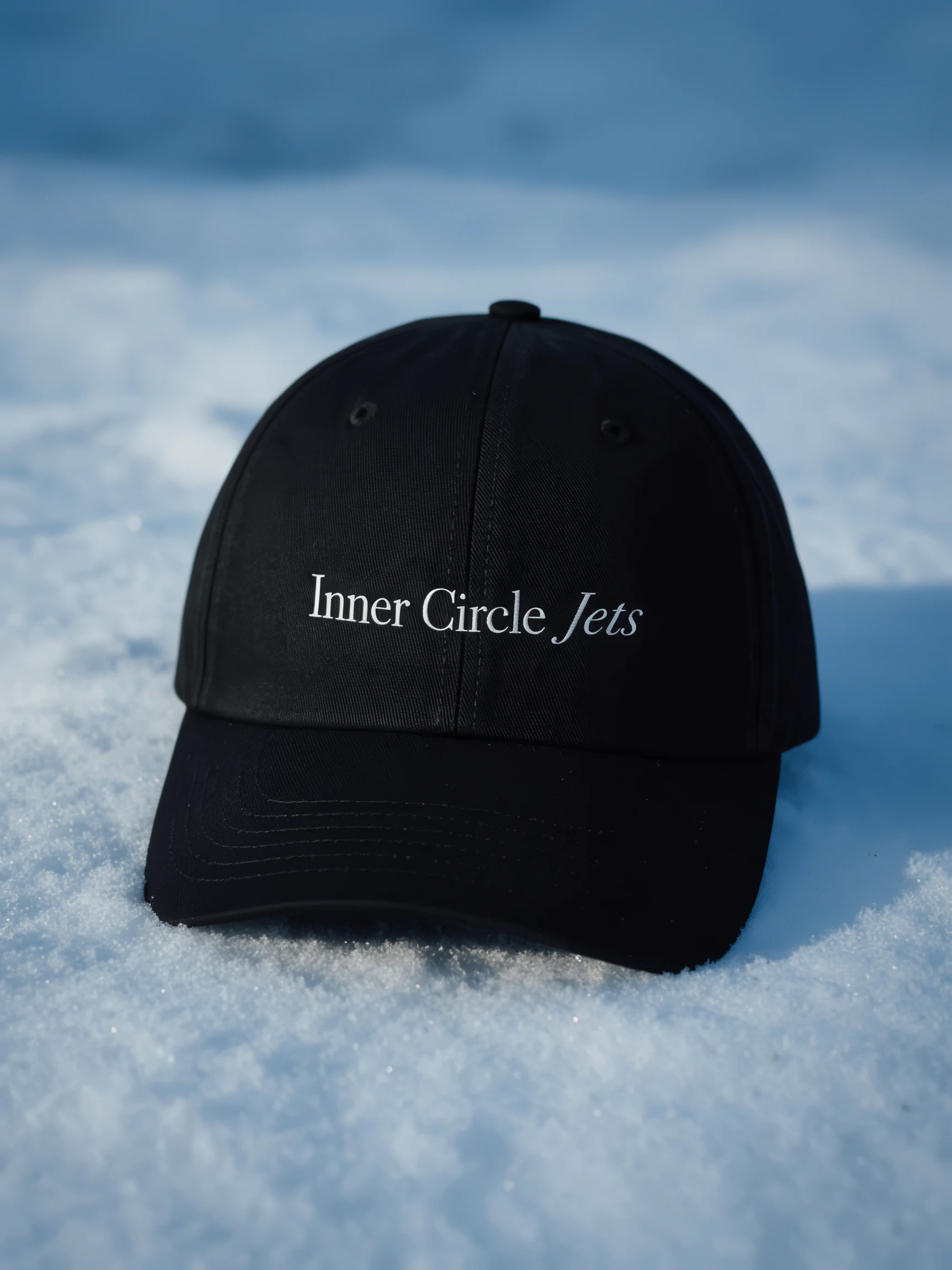 A black Inner Circle Jets cap resting in snow