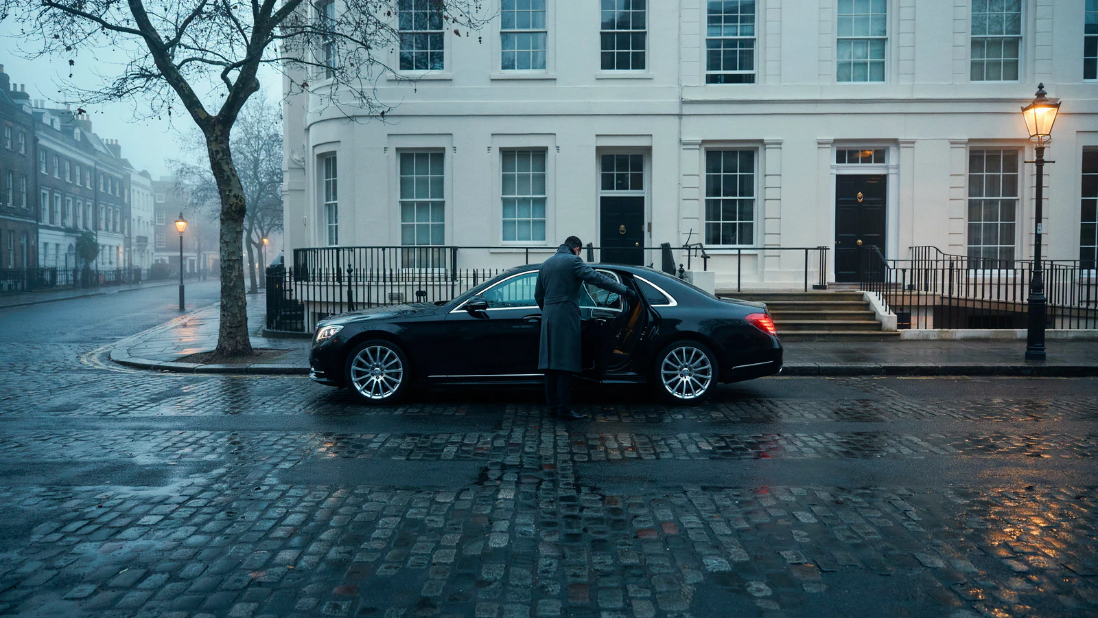 A chauffeur opening a car door outside a London townhouse at dawn