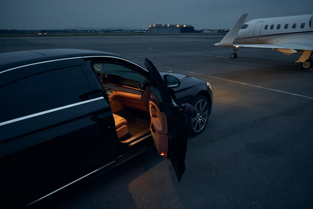 A chauffeured car waiting beside a private jet at dusk